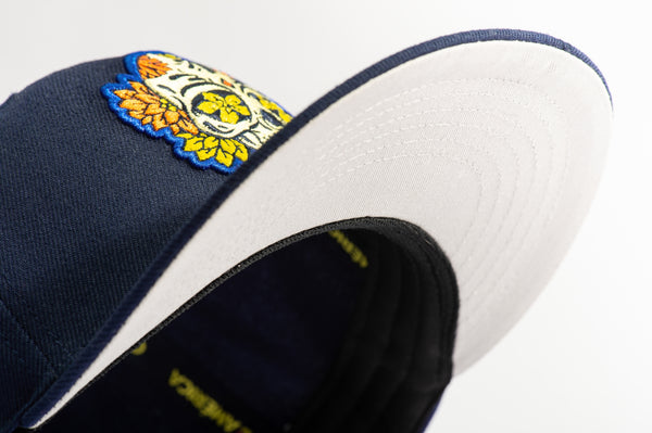 Club America Day of the Dead Snapback Hat with floral skull embroidered on the front, Club America embroidered on the side, "Dia de Muertos" embroidered on the back. The hat has a high crown, flat peak brim, and a snapback closure.