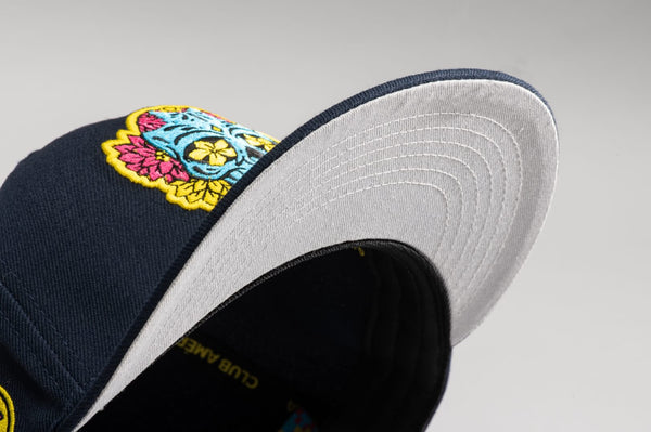 Club America Day of the Dead Snapback Hat with floral skull embroidered on the front, Club America embroidered on the side, "Dia de Muertos" embroidered on the back. The hat has a high crown, flat peak brim, and a snapback closure.